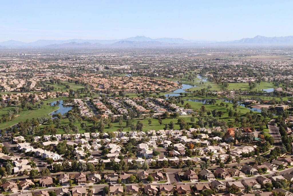 An aerial view of a suburban neighborhood in Chandler, Arizona, featuring golf courses, lakes, and residential communities with desert mountain ranges in the background.